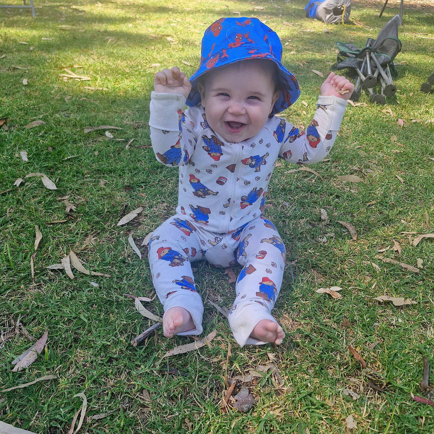 Walter is registered to the contest to win money with this photo: baby, barefoot, bucket_hat, cartoon_print, child, clothing, daylight, grass, greenery, happy, hat, nature, onesie, outdoor, park, person, playful, sitting, smiling, sunlight