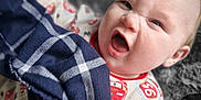 Walter is registered to the contest to win money with this photo: baby, child, infant, blanket, plaid, onesie, clothing, face, expression, funny_face, holding, soft_surface, patterned_clothing, indoor, portrait, cute, scrunched_face, young_child, fabric, closeup