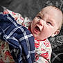 baby, child, infant, blanket, plaid, onesie, clothing, face, expression, funny_face, holding, soft_surface, patterned_clothing, indoor, portrait, cute, scrunched_face, young_child, fabric, closeup