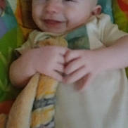 Emmett is registered to the contest to win money with this photo: baby, infant, smiling, blurry, blanket, playmat, hands, bald_head, onesie, portrait, close_up, cheerful, soft_blanket, fabric, indoor, seated, colorful_background, cute, human, small_child