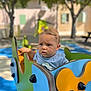Milann a rejoint le concours — aidez-le/la à gagner de superbes lots ! toddler, child, playground, outdoor, ride, colorful, flower, blue_shirt, curious, face, expression, sunny, trees, bench, building, play_area, young_child, daylight, person, park
