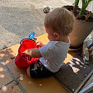Milann a rejoint le concours — aidez-le/la à gagner de superbes lots ! toddler, child, bucket, plant, sandals, tiles, dirt, outdoor, blonde_hair, white_shirt, black_shorts, sitting, playing, side_view, daylight, shadow, doorway, curly_hair, potted_plant, footwear