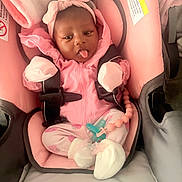 Jriyah is registered to the contest to win money with this photo: baby, infant, car_seat, pink_clothing, headband, mittens, socks, pacifier, baby_accessory, child, cute, playful, sticking_tongue, seat_belt, soft_toys, indoor, newborn, portrait, person, baby_girl