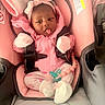 baby, infant, car_seat, pink_clothing, headband, mittens, socks, pacifier, baby_accessory, child, cute, playful, sticking_tongue, seat_belt, soft_toys, indoor, newborn, portrait, person, baby_girl