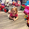 toddler, child, smiling, happy, portrait, playroom, toys, toy_cars, tricycle, ride_on_toy, stuffed_animal, plush_sheep, toy_phone, toy_chair, buckets, indoor, floor, sitting, blonde_hair, colorful