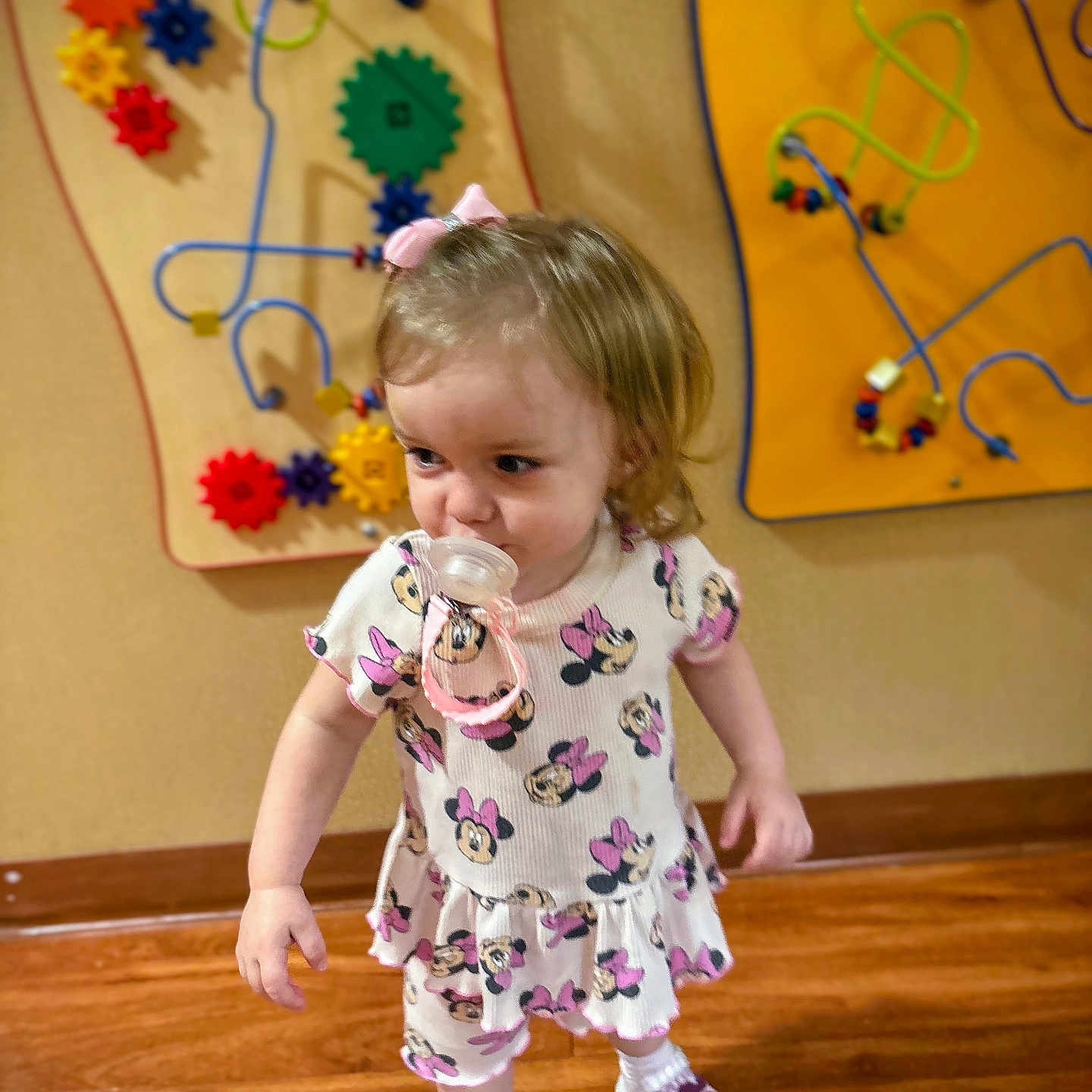 Barbie Rae joined the competition — help win amazing prizes! blonde_hair, bow, child, colorful, cute, dress, gears, indoor, minnie_mouse, pacifier, person, playroom, shoes, socks, toddler, toys, walking, wall_toys, wooden_floor, young_child