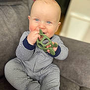Malaki is registered to the contest to win money with this photo: baby, child, teether, toy, blue_eyes, striped_clothing, onesie, couch, gray_couch, indoor, smiling, happy, sitting, infant, cute, chewing, hand, face, skin, young_child