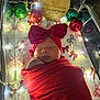 newborn, baby, sleeping, red_bow, red_blanket, crib, christmas_ornaments, fairy_lights, festive, holiday, infant, swaddled, face, headband, peaceful, decorations, closeup, portrait, cute, indoors