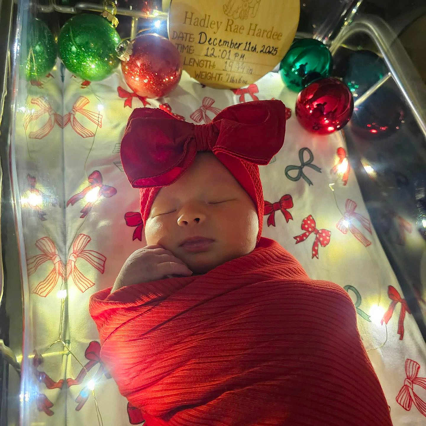 Hadley joined the competition — help win amazing prizes! baby, christmas_ornaments, closeup, crib, cute, decorations, face, fairy_lights, festive, headband, holiday, indoors, infant, newborn, peaceful, portrait, red_blanket, red_bow, sleeping, swaddled