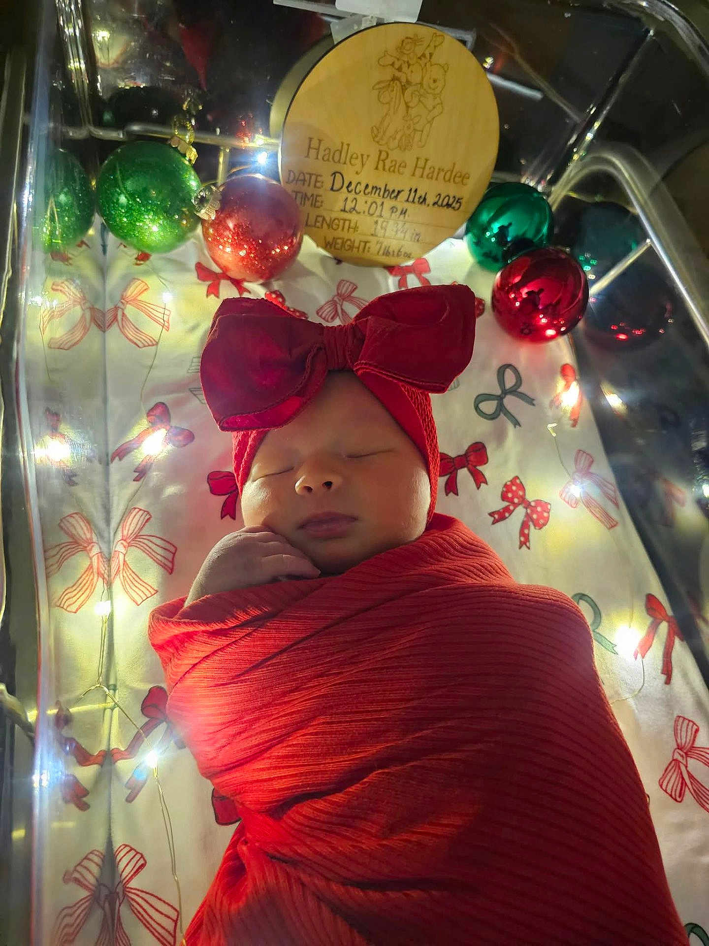 Hadley joined the competition — help win amazing prizes! newborn, baby, sleeping, red_bow, red_blanket, crib, christmas_ornaments, fairy_lights, festive, holiday, infant, swaddled, face, headband, peaceful, decorations, closeup, portrait, cute, indoors