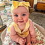 baby, infant, smiling, blue_eyes, headband, bow, yellow_outfit, chubby_cheeks, sitting, hands, toes, floral_pattern, blanket, playpen, living_room, carpet, wooden_furniture, portrait, close_up, cute