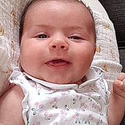 Leonie participe au concours pour gagner de l'argent avec cette photo : baby, child, smiling, infant, white_dress, patterned_clothing, blanket, cushion, green_pillow, indoor, cute, happy, person, face, head, young_child, soft_texture, resting, closeup, comfortable