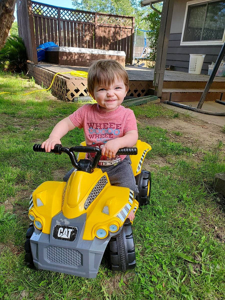 Carsyn is registered to the contest to win money with this photo: backyard, child, garden, grass, lawn, outdoor_power_equipment, person, plant, riding_mower, riding_toy, toddler, tool, vehicle, yard