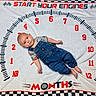 baby, infant, child, portrait, lying_down, smiling, wide_eyed, denim_overalls, clothing, race_car_theme, milestone_blanket, speedometer, numbers, checkered_pattern, red_text, white_blanket, indoor, photography, cute, month milestone