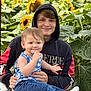 child, young_adult, smiling, sunflower, flower_field, outdoor, hoodie, jeans, wicker_chair, nature, greenery, happy, casual_clothing, portrait, family, holding, sitting, daylight, plants, people