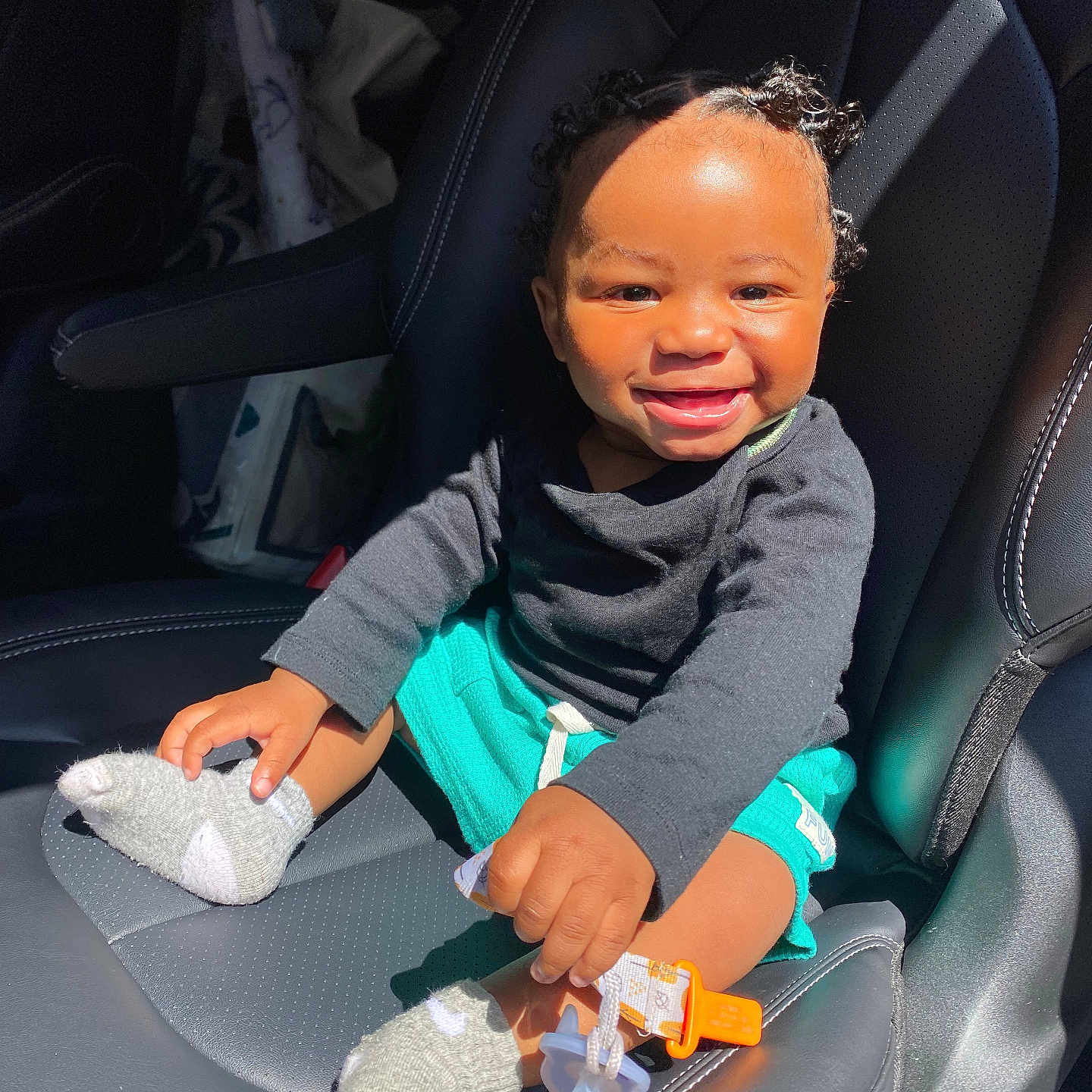 Esseny joined the competition — help win amazing prizes! baby, black_shirt, bright, car_seat, child, comfort, curly_hair, cute, happy, holding, infant, interior, pacifier, playful, seat, smiling, sock, sunlight, teal_shorts, toddler