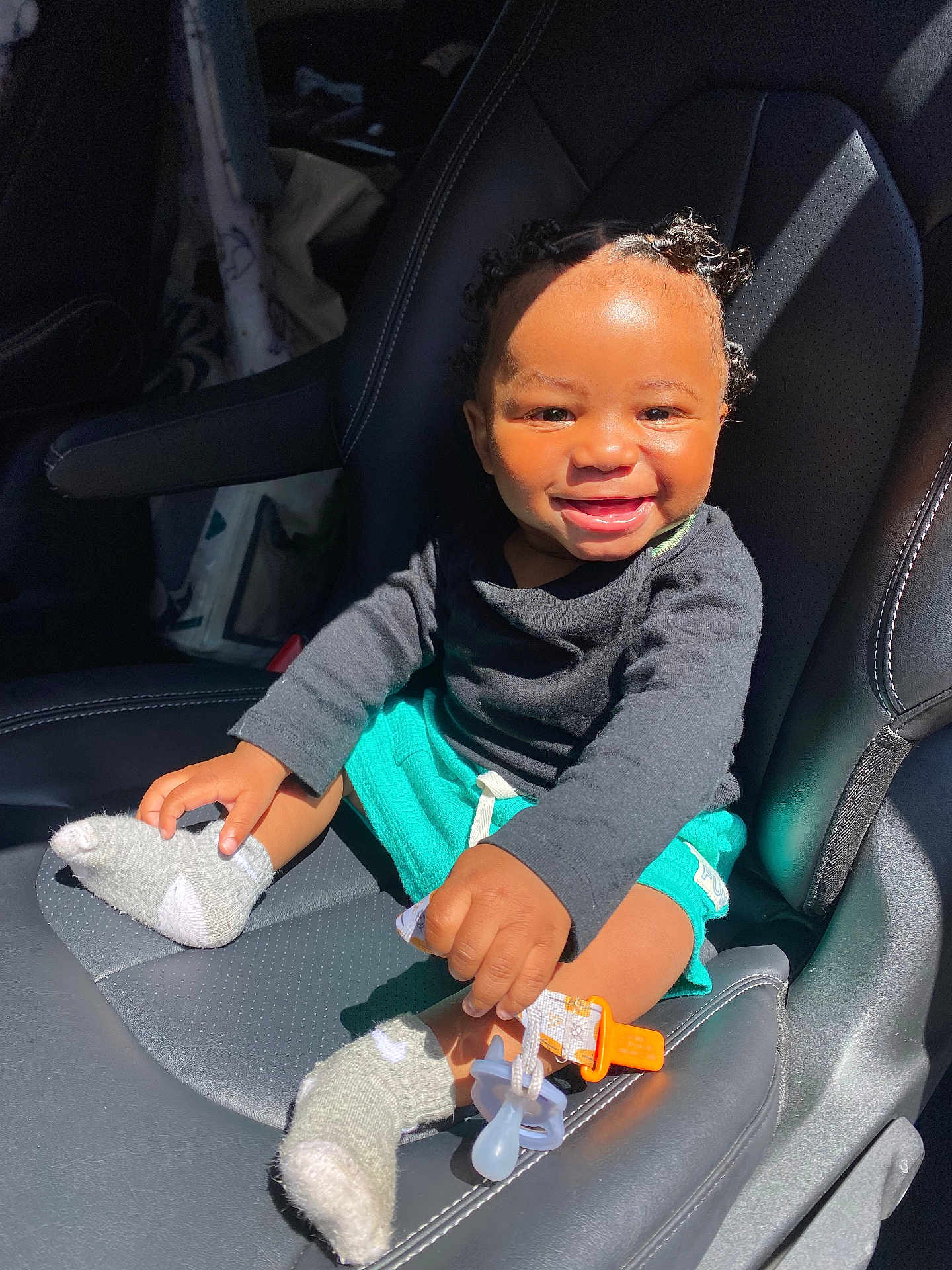 Esseny joined the competition — help win amazing prizes! toddler, child, smiling, car_seat, pacifier, sock, curly_hair, black_shirt, teal_shorts, sunlight, happy, baby, seat, interior, cute, holding, comfort, infant, playful, bright