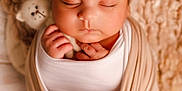 Cyrus is registered to the contest to win money with this photo: baby, sleeping, newborn, swaddled, hat, knit, stuffed_animal, toes, soft_lighting, cozy, cute, infant, peaceful, wrapped, child, portrait, closeup, warm_colors, hands, face
