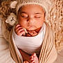 baby, sleeping, newborn, swaddled, hat, knit, stuffed_animal, toes, soft_lighting, cozy, cute, infant, peaceful, wrapped, child, portrait, closeup, warm_colors, hands, face