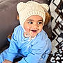 Cyrus is registered to the contest to win money with this photo: child, toddler, smiling, hat, knitted_hat, blue_outfit, sitting, indoor, couch, toy, happy, cute, face, person, young_child, patterned_pillow, cozy, warm_clothing, playful, portrait