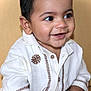 Cyrus is registered to the contest to win money with this photo: baby, child, smiling, happy, face, portrait, indoor, clothing, white_shirt, embroidered, cute, infant, young_child, skin, head, eyes, mouth, expression, sitting, person
