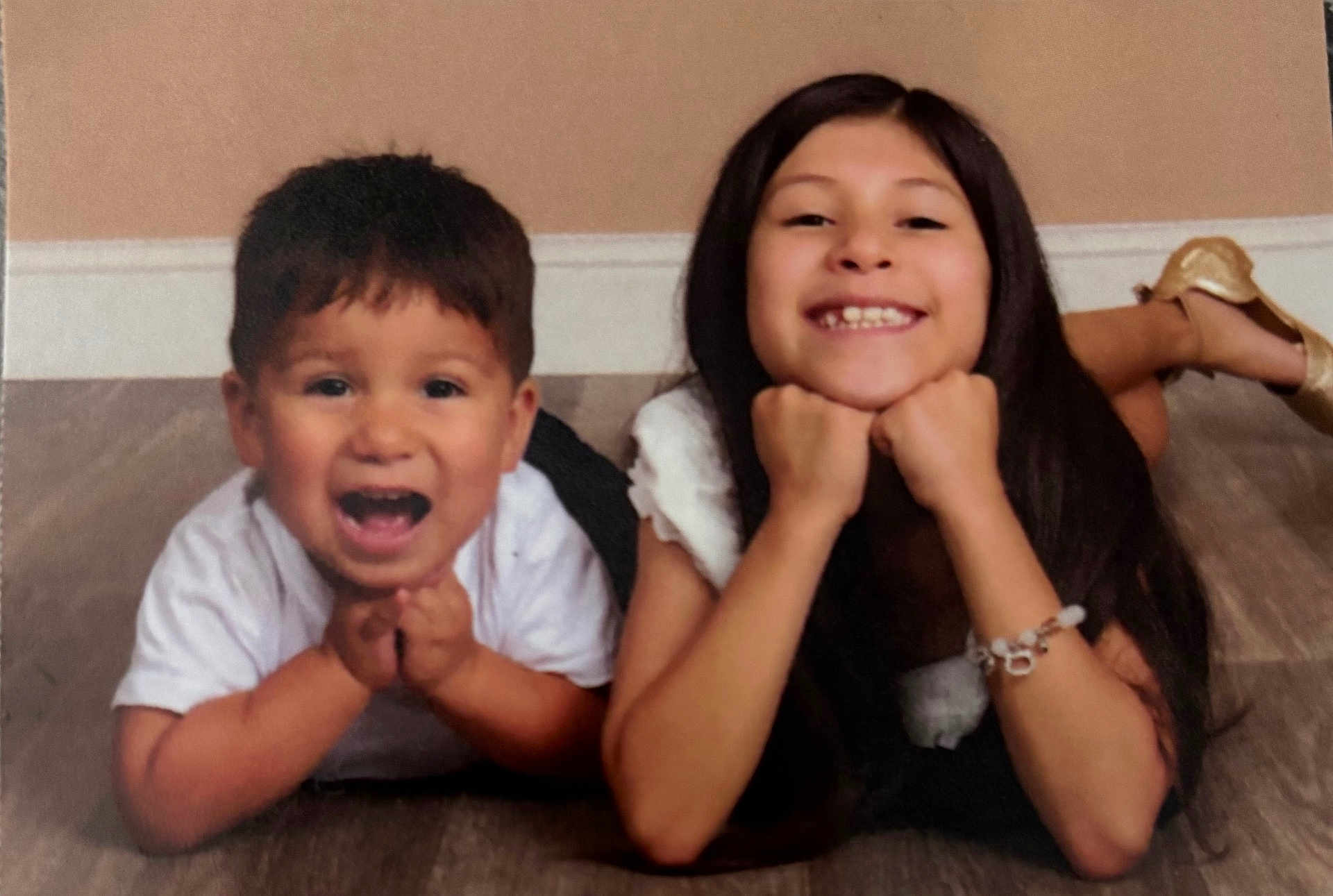 Isaiah Ramos is registered to the contest to win money with this photo: child, kids, smiling, happy, floor, portrait, siblings, playful, casual, indoor, young, person, cute, hands, face, long_hair, short_hair, shoe, bracelet, white_shirt