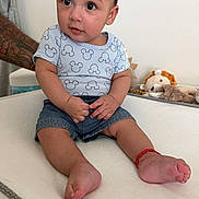 Alejandro joined the competition — help win amazing prizes! baby, child, infant, mickey_mouse, shirt, denim_shorts, tattoo, arm, plush_toys, toy_lion, toy_dog, sitting, curious_expression, indoor, white_background, red_bracelet, barefoot, person, cute, portrait