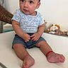 baby, child, infant, mickey_mouse, shirt, denim_shorts, tattoo, arm, plush_toys, toy_lion, toy_dog, sitting, curious_expression, indoor, white_background, red_bracelet, barefoot, person, cute, portrait