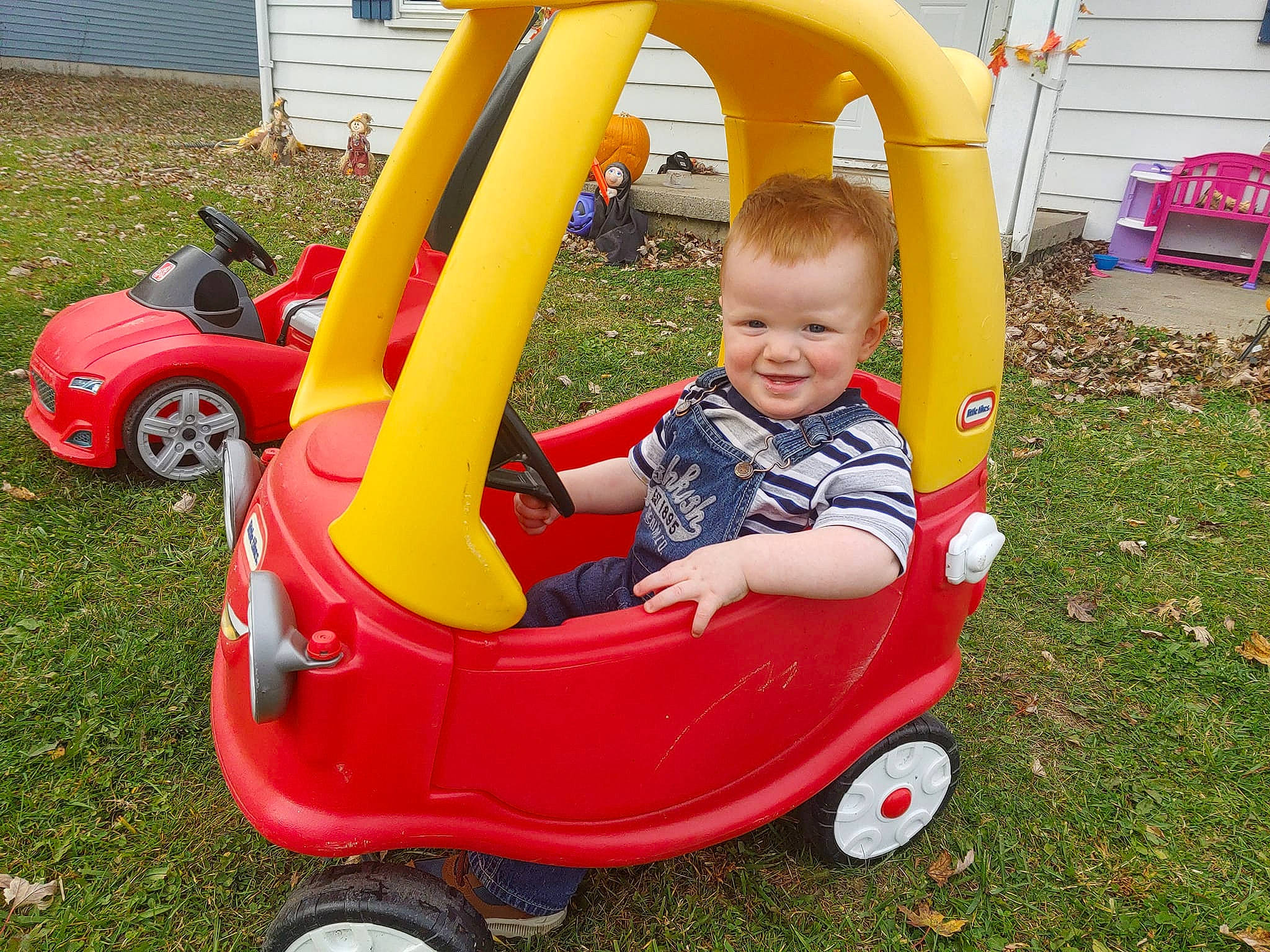 Keanu is registered to the contest to win money with this photo: automotive_design, automotive_wheel_system, baby_toddler_clothing, car, chair, face, fun, grass, joy, leisure, motor_vehicle, person, plant, recreation, riding_toy, shorts, smile, tire, toddler, vehicle