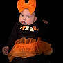 baby, child, halloween, costume, orange_bow, tutu, black_background, cute, festive, pumpkin_face, ghost_graphic, long_sleeve_shirt, leggings, portrait, indoor, chubby_cheeks, headband, holiday, smiling, infant