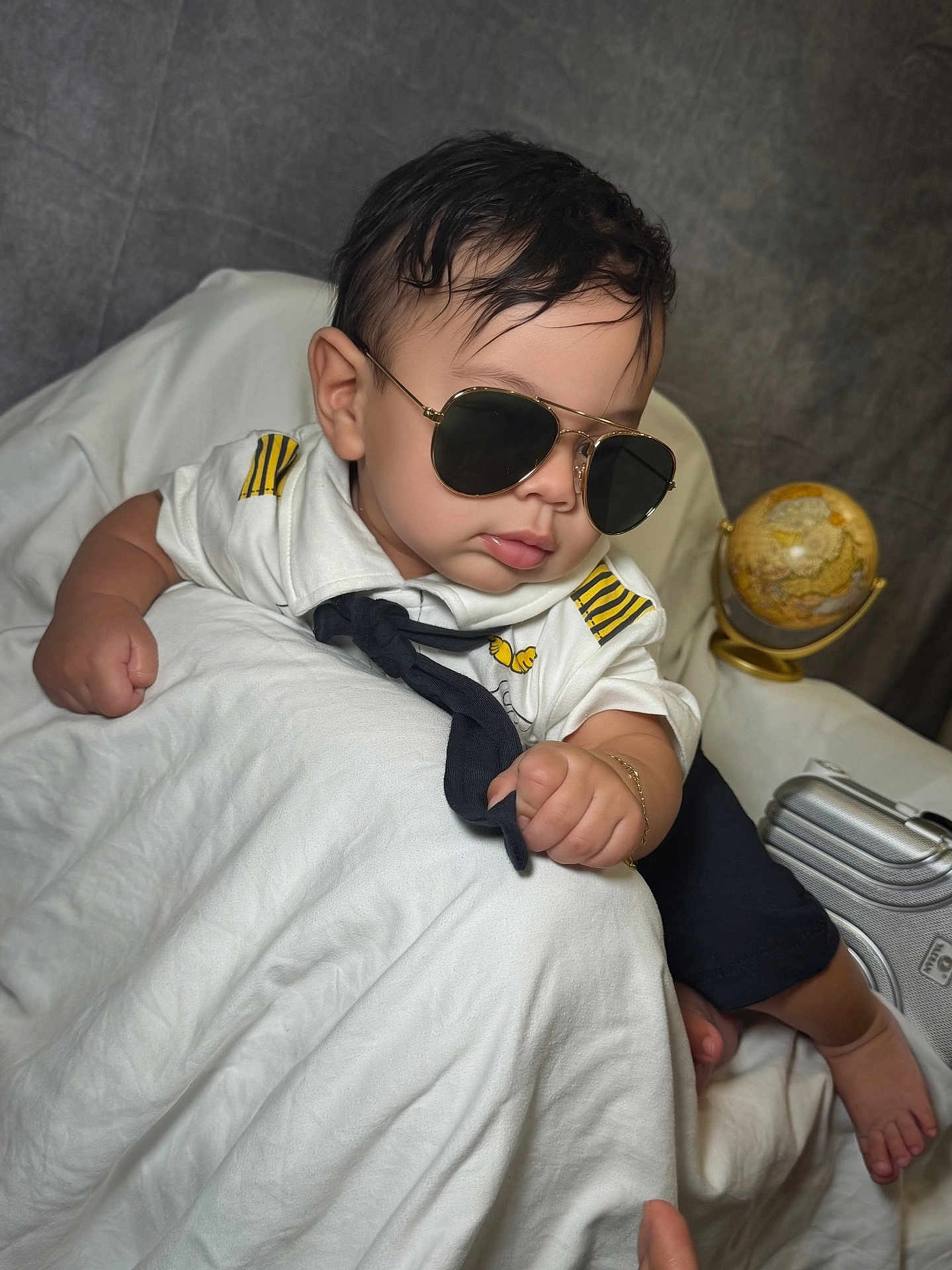 Elian joined the competition — help win amazing prizes! baby, child, sunglasses, pilot_uniform, white_cloth, globe, suitcase, indoor, portrait, cute, fashion, accessory, person, infant, hand, foot, black_hair, tie, bracelet, seat