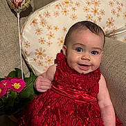 Amelia joined the competition — help win amazing prizes! baby, infant, smiling, red_dress, sequined_dress, sitting, couch, floral_pillow, balloon, love_balloon, pink_flowers, potted_plant, portrait, blue_eyes, rosy_cheeks, hand, fabric, cute, indoor, close_up