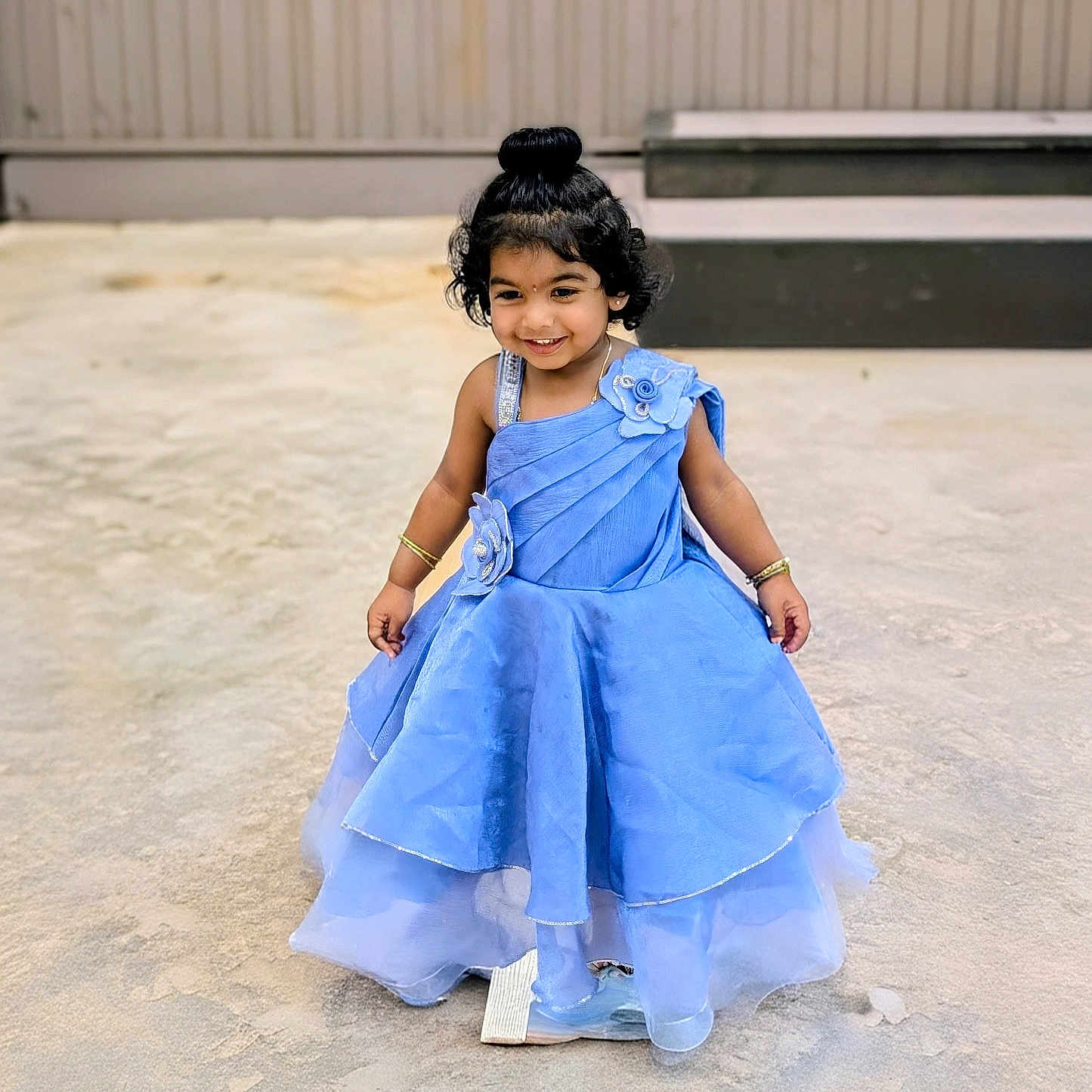 Aishani Ponaka joined the competition — help win amazing prizes! child, toddler, blue_dress, smile, happy, outdoor, sandy_ground, curly_hair, hair_bun, bracelet, flower_decoration, dress, person, fashion, portrait, cute, standing, accessories, young, celebration