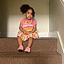 child, toddler, girl, stairs, carpet, dress, pink_shoes, curly_hair, indoor, smiling, sitting, young_child, playful, fashion, casual, person, portrait, accessories, cute, happy