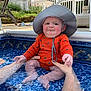 Mason joined the competition — help win amazing prizes! baby, child, pool, water, orange_clothing, sunhat, hands, backyard, fence, grass, summer, expression, outdoor, funny_face, sitting, skin, person, sunlight, blue, swimsuit