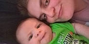 Mason is registered to the contest to win money with this photo: baby, adult, face, smile, green_shirt, text_on_clothing, closeup, indoor, portrait, skin, head, person, child, happy, cuddle, casual, bonding, family, toddler, clothing