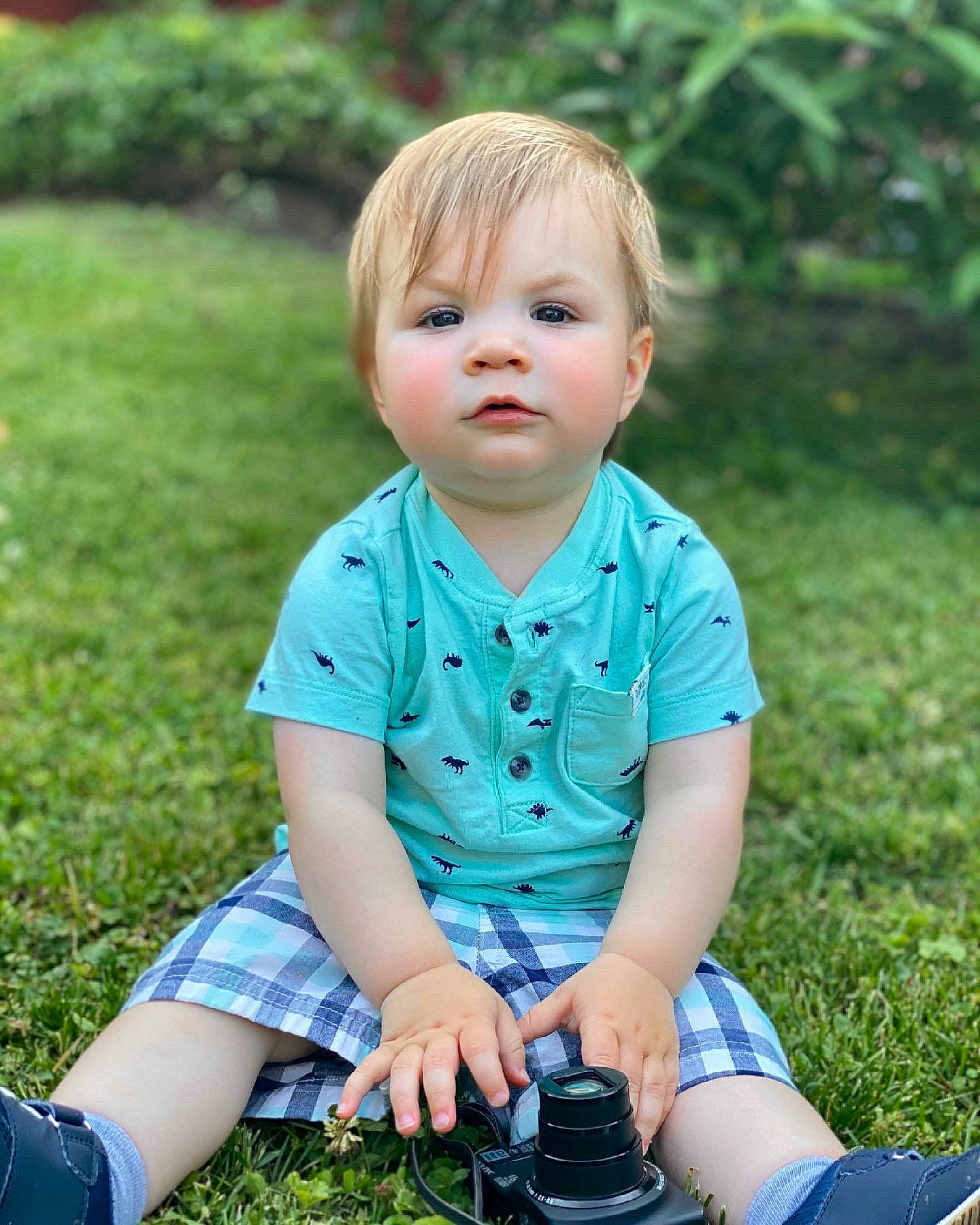 Simon is registered to the contest to win money with this photo: baby_toddler_clothing, camera, eye, face, fun, grass, grass_family, green, happy, head, lawn, people_in_nature, person, photograph, plant, reflex_camera, sleeve, sneakers, summer, t_shirt
