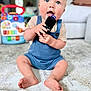 Owen is registered to the contest to win money with this photo: baby, child, remote_control, blue_overalls, carpet, indoor, toy, couch, floor, chewing, hands, feet, face, person, curious, sitting, blond_hair, wide_eyes, home, blurred_background