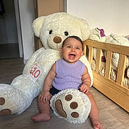 Kayana a rejoint le concours — aidez-le/la à gagner de superbes lots ! baby, smiling_baby, teddy_bear, stuffed_animal, crib, wooden_floor, purple_sweater, sitting, chubby_legs, happy, indoor, plush_paw, milestone_card, cute, portrait, nursery, soft_toy, playful, cozy, child