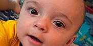 Asher is registered to the contest to win money with this photo: baby, bed, blanket, child, closeup, curious, expression, eyes, face, foot, head, human, indoor, mouth, person, portrait, room, skin, television, yellow_shirt