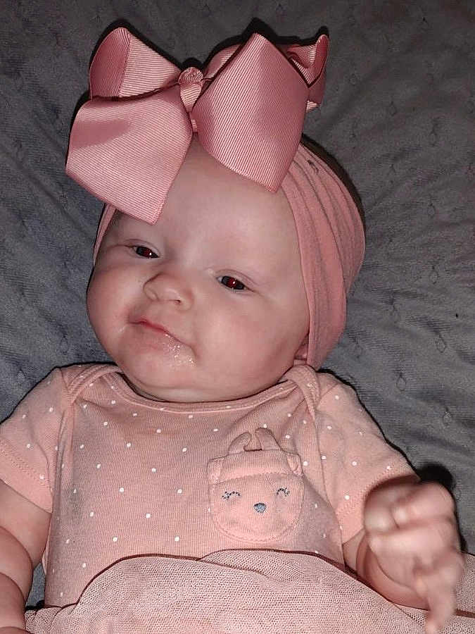 Adalynn is registered to the contest to win money with this photo: baby, infant, pink, headband, bow, clothing, face, portrait, cute, drool, lying_down, soft_texture, child, young, apparel, fabric, closeup, skin, smile, adorable