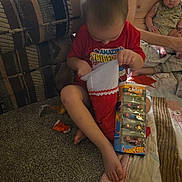 Joseph is registered to the contest to win money with this photo: child, baby, adult, couch, carpet, christmas_stocking, toy, hot_wheels, person, indoor, family, red_shirt, spiderman, sitting, curious, floor, holding, blanket, home, play