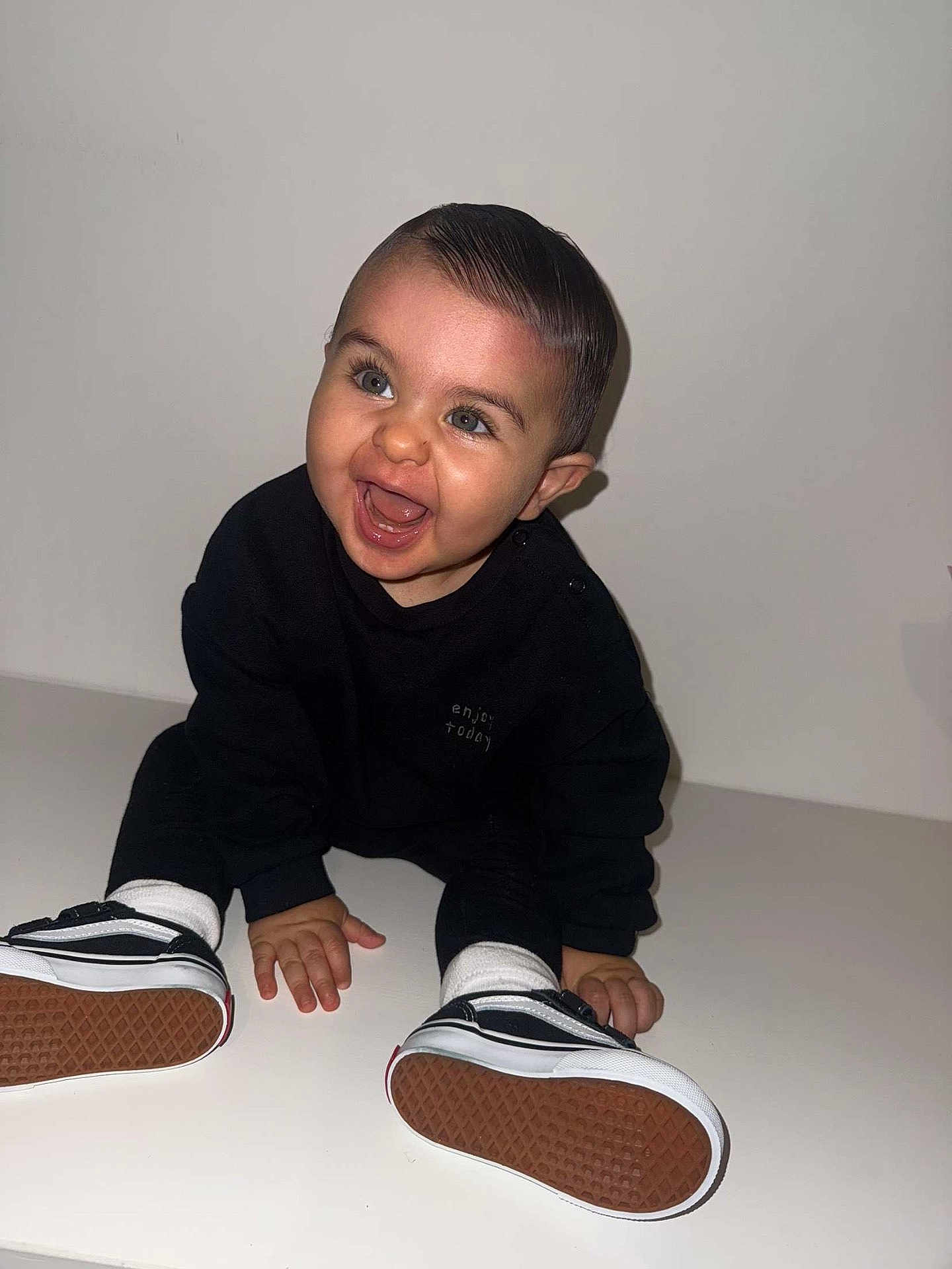 Isaac participe au concours pour gagner de l'argent avec cette photo : baby, child, smiling, sitting, black_clothing, white_socks, sneakers, happy, indoor, portrait, cute, young_child, face, hands, feet, white_background, studio, fashion, expression, infant