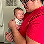 Domenic is registered to the contest to win money with this photo: baby, adult, holding, indoor, red_shirt, glasses, curious, infant, person, portrait, love, family, casual_clothing, face, skin, hair, hand, expression, home, comfort