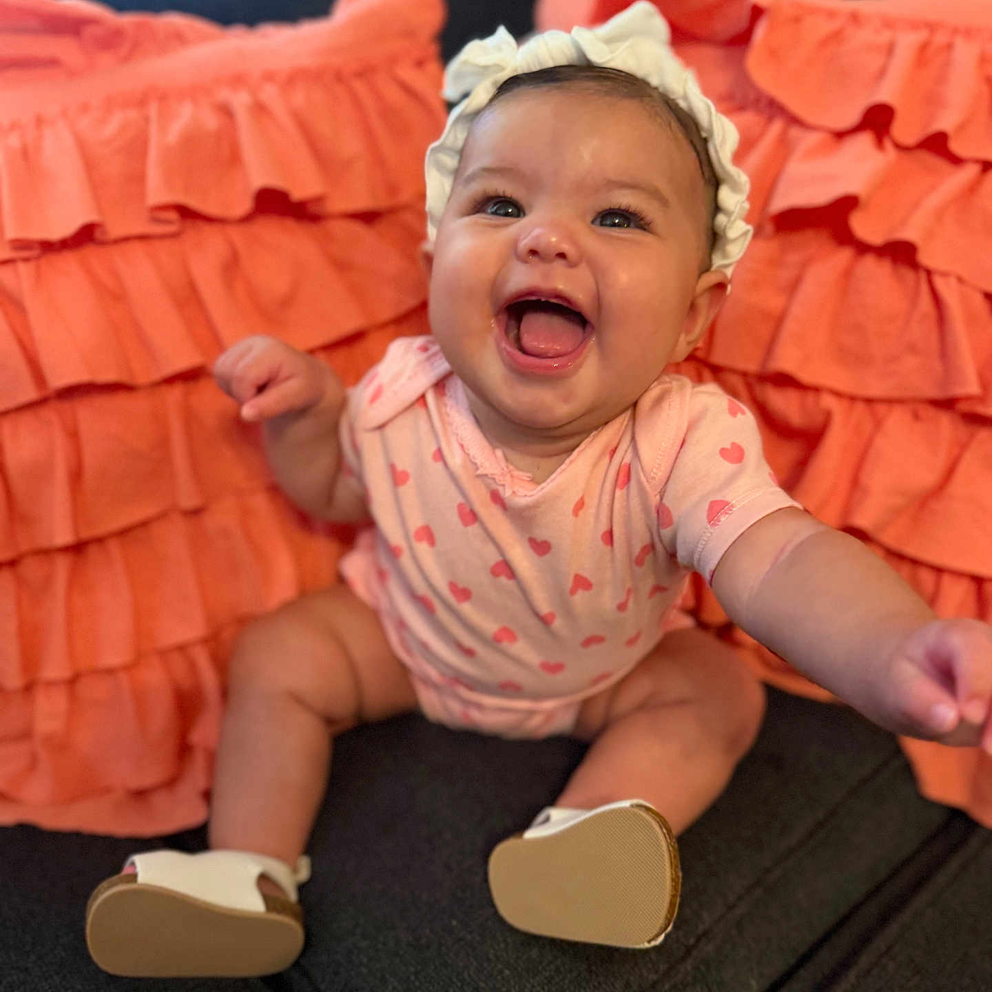 Alaiyah joined the competition — help win amazing prizes! baby, infant, smiling, happy, onesie, headband, couch, pillow, orange, pink, clothing, footwear, indoor, furniture, person, cute, child, portrait, sitting, expression