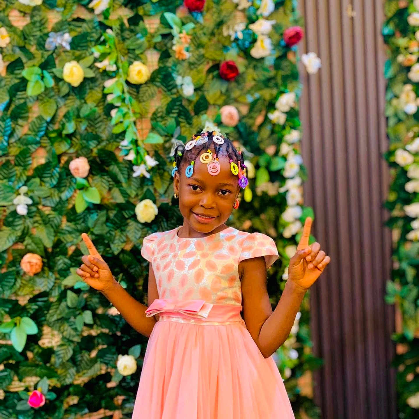 Fatim participe au concours pour gagner de l'argent avec cette photo : background, braids, celebration, child, colorful, dress, fashion, flower_wall, flowers, girl, greenery, hair_accessories, happy, nature, outdoor, pink_dress, playful, portrait, posing, smiling
