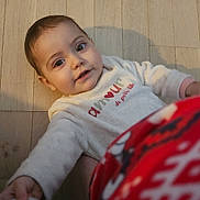 Emma a rejoint le concours — aidez-le/la à gagner de superbes lots ! baby, child, floor, wooden_floor, sweater, text_on_clothing, indoor, person, cute, infant, reaching, curious, face, head, smiling, long_sleeves, red_pattern, warm_clothing, lying_down, young_child