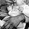 baby, feeding, hand, adult, toy, black_and_white, infant, clothing, sitting, closeup, face, mouth, curious, gentle, parent, care, trust, cute, interaction, domestic