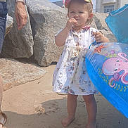 Lorenza Ouin a rejoint le concours — aidez-le/la à gagner de superbes lots ! toddler, child, beach, sand, inflatable, float, cap, dress, barefoot, adult, rocks, building, sky, sunny, outdoor, summer, playful, vacation, holiday, person