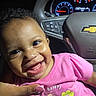 baby, child, infant, smiling, happy, portrait, car, car_interior, car_seat, dashboard, steering_wheel, pink_shirt, floral_design, flowers, teeth, curly_hair, close_up, indoor, daylight, family_photo